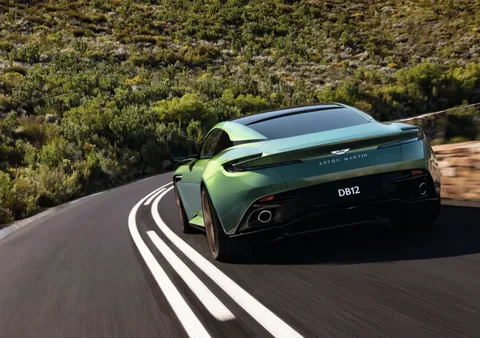 A green Aston Martin DB12 driving along a winding mountain road.